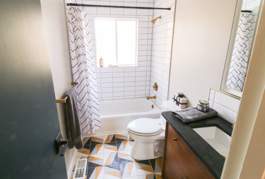 Millie's remodel bathroom, white stacked subway tile around white tub gold finishes and black and yellow houndstooth floor pattern