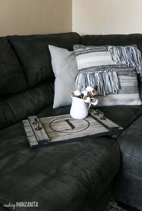 rustic wood serving tray on black couch, pillows in background