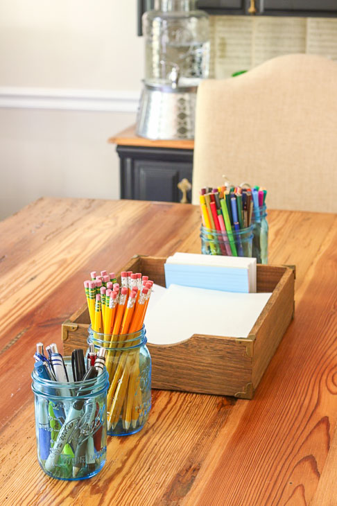 dining room table set with homework supplies pencils, paper, pens